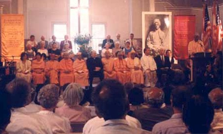 Visiting Swamis, religious leaders of different faiths, and musical artists seated in front of a crowd.