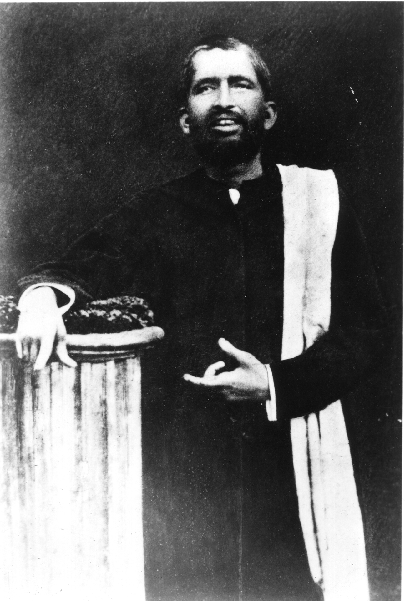 Black and white photo of Sri Ramakrishna leaning on a column.