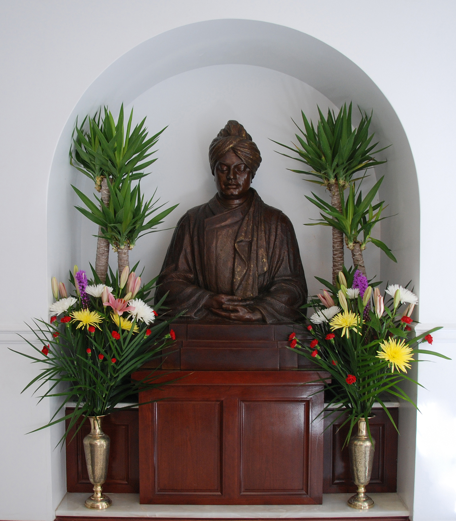 Metal sculpture of Swami Vivekananda seated surrounded by flowers.