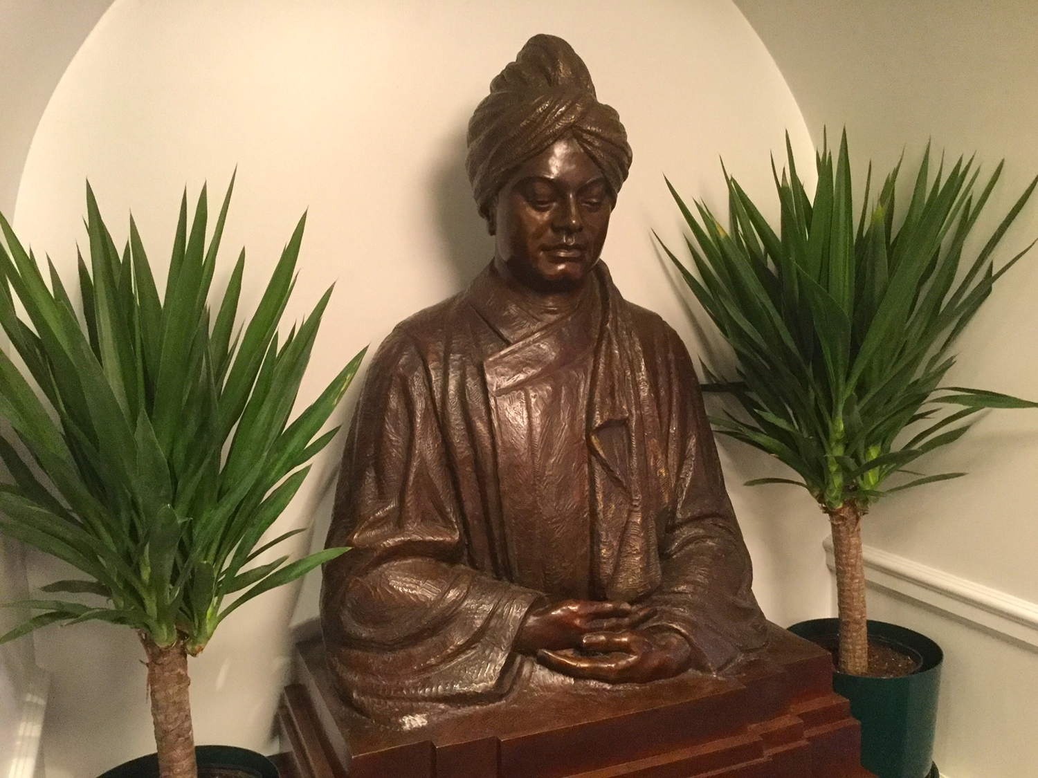 Metal sculpture of Swami Vivekananda seated surrounded by flowers.