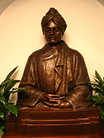 Metal sculpture of Swami Vivekananda seated surrounded by flowers.